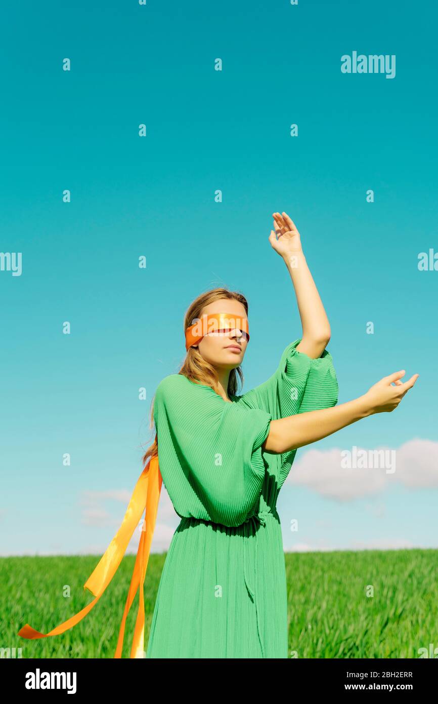 Giovane donna bendata che indossa un vestito verde in piedi in un campo Foto Stock