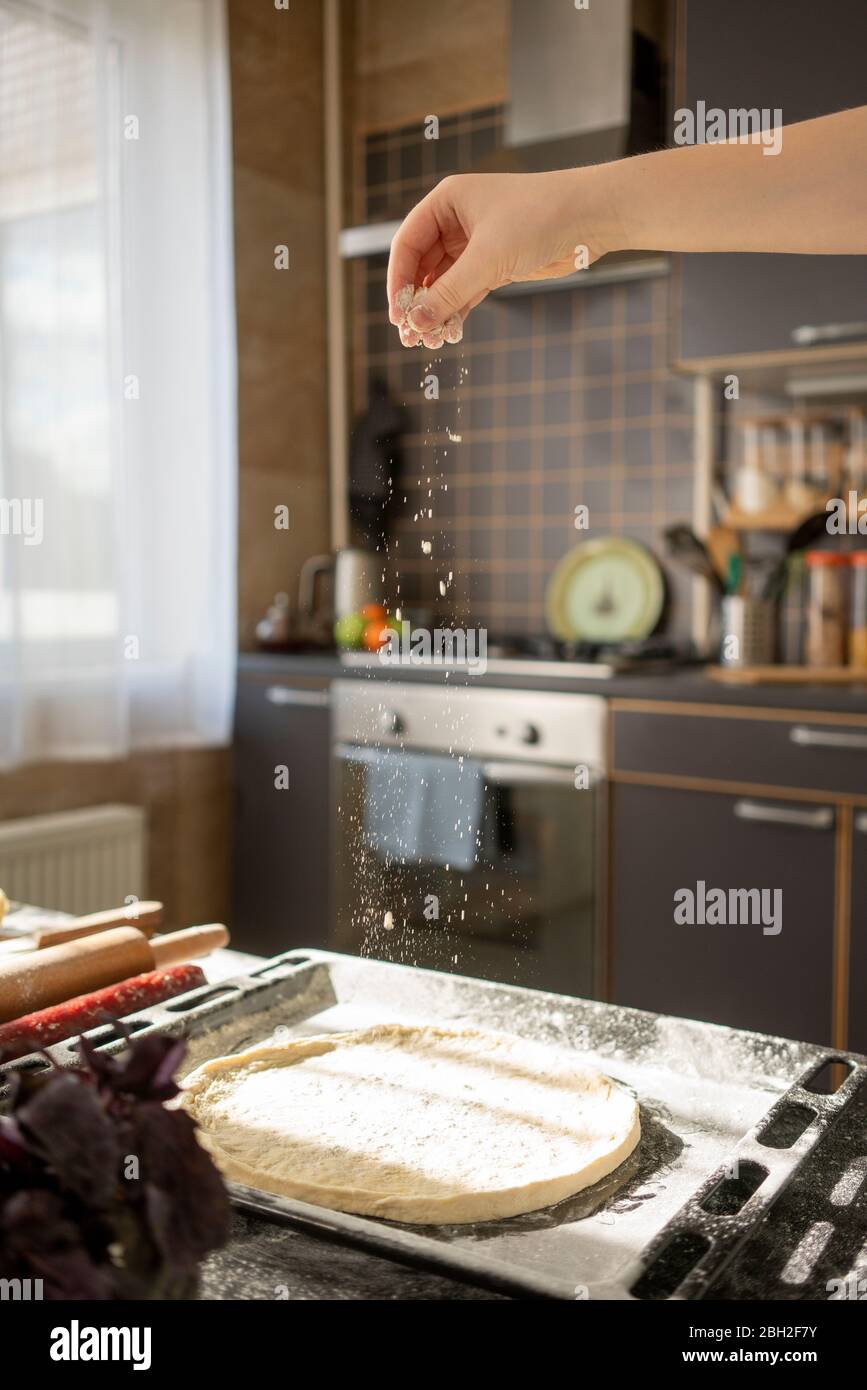 La mano del ragazzo che spara la farina sulla base della pizza Foto Stock