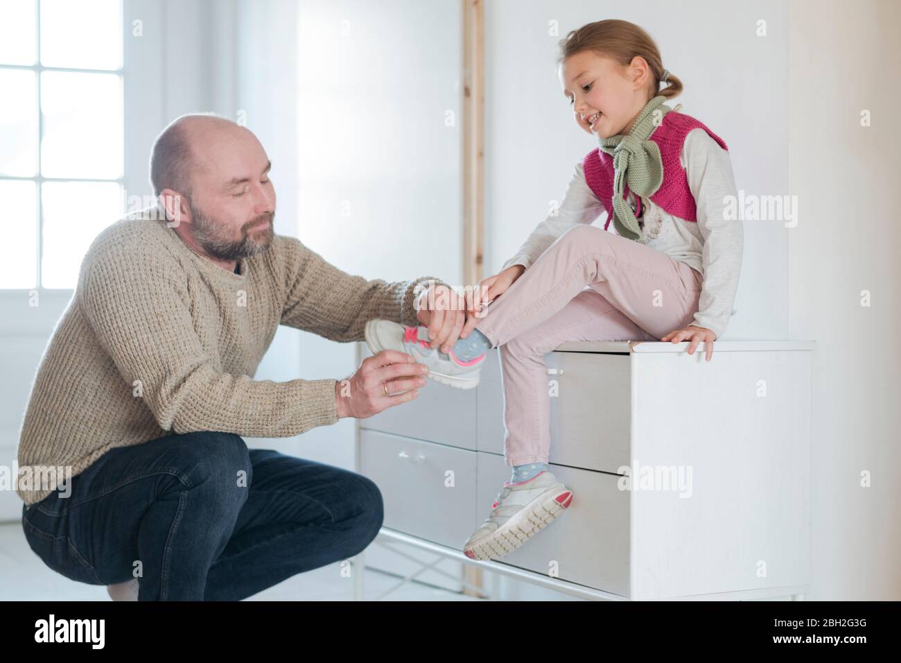 Padre che aiuta la figlia a indossare scarpe a casa Foto Stock