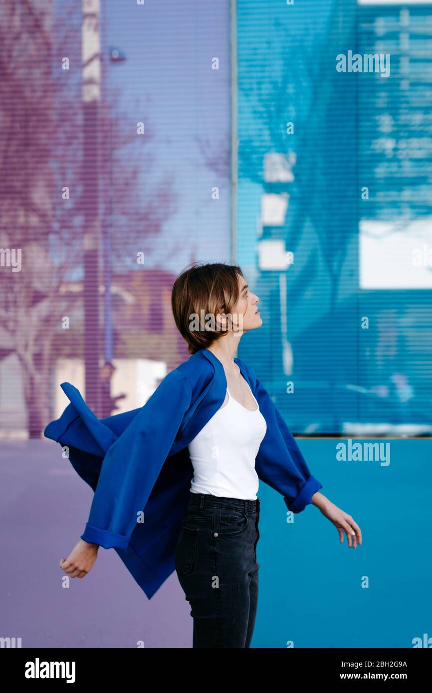 Ritratto di giovane donna che gioca con il movimento della giacca di fronte a una parete di vetro colorato Foto Stock