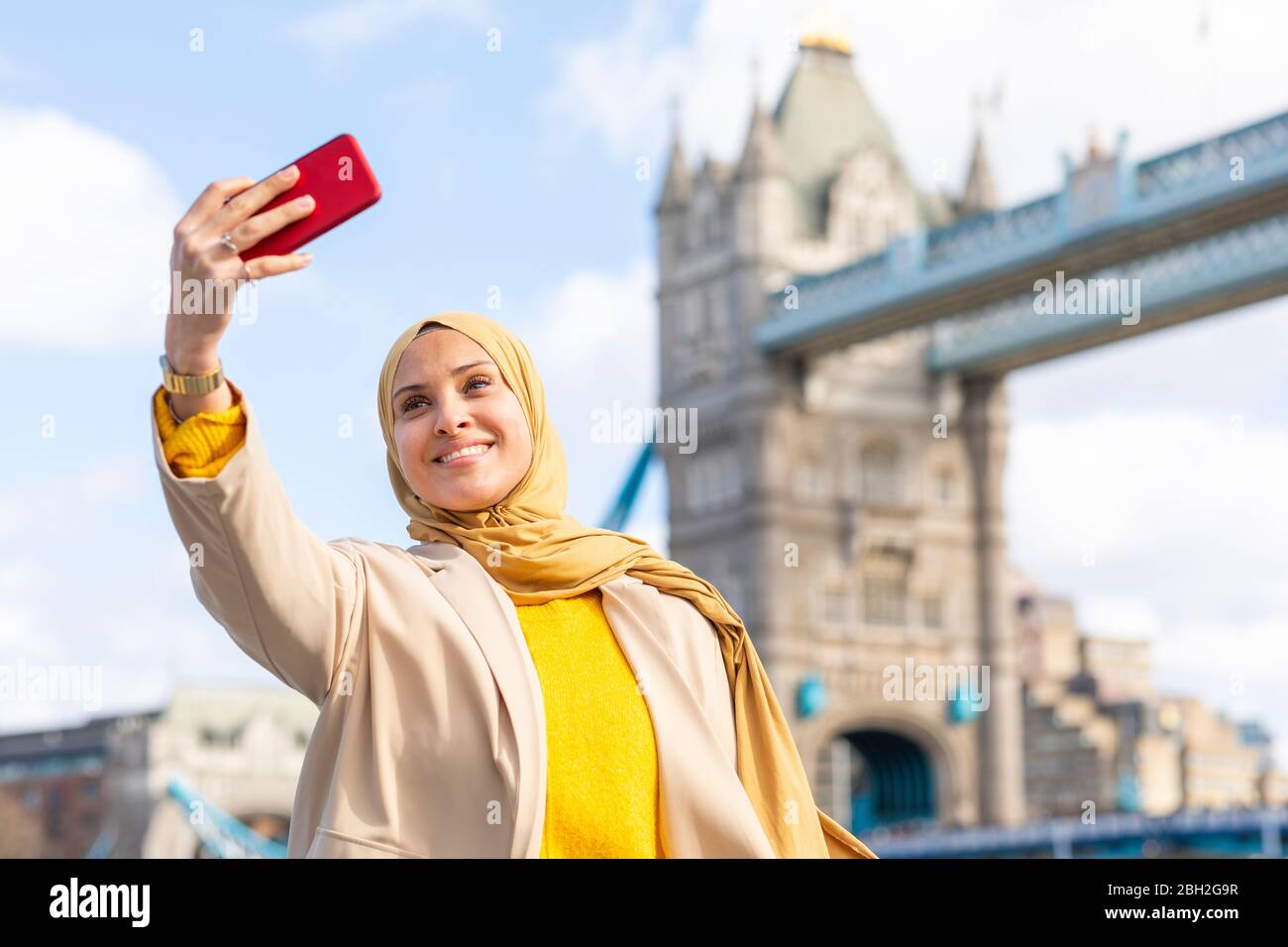 Ritratto di giovane donna sorridente che prende selfie con smartphone di fronte a Tower Bridge, Londra, Regno Unito Foto Stock