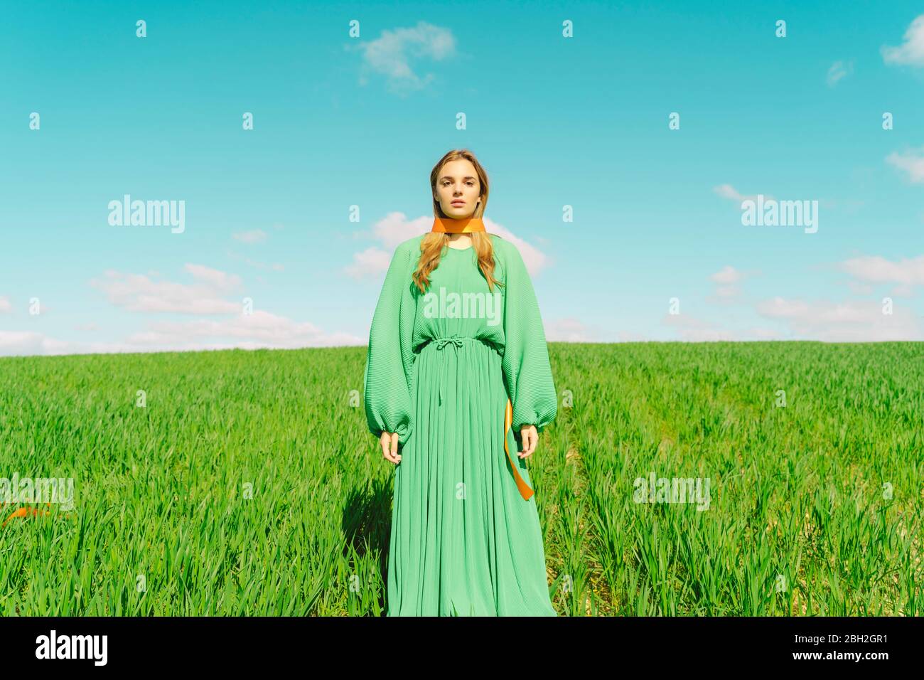 Ritratto di giovane donna che indossa un vestito verde in piedi in un campo con un nastro intorno al collo Foto Stock