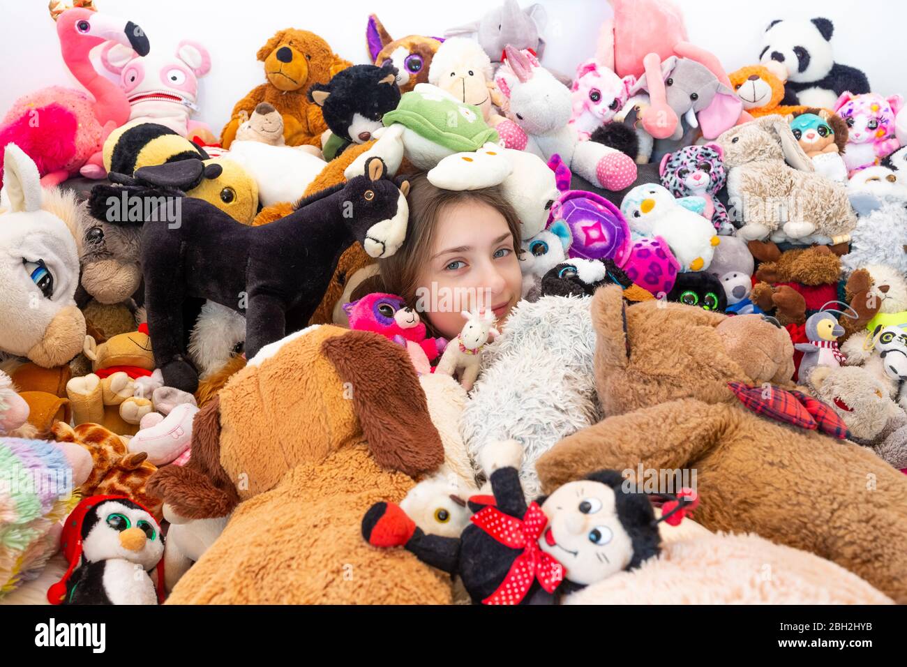 Ragazza seduta sul divano, coperta di giocattoli coccolati Foto Stock