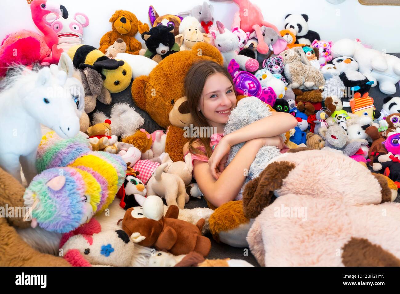 Ragazza seduta sul divano, coperta di giocattoli coccolati Foto Stock