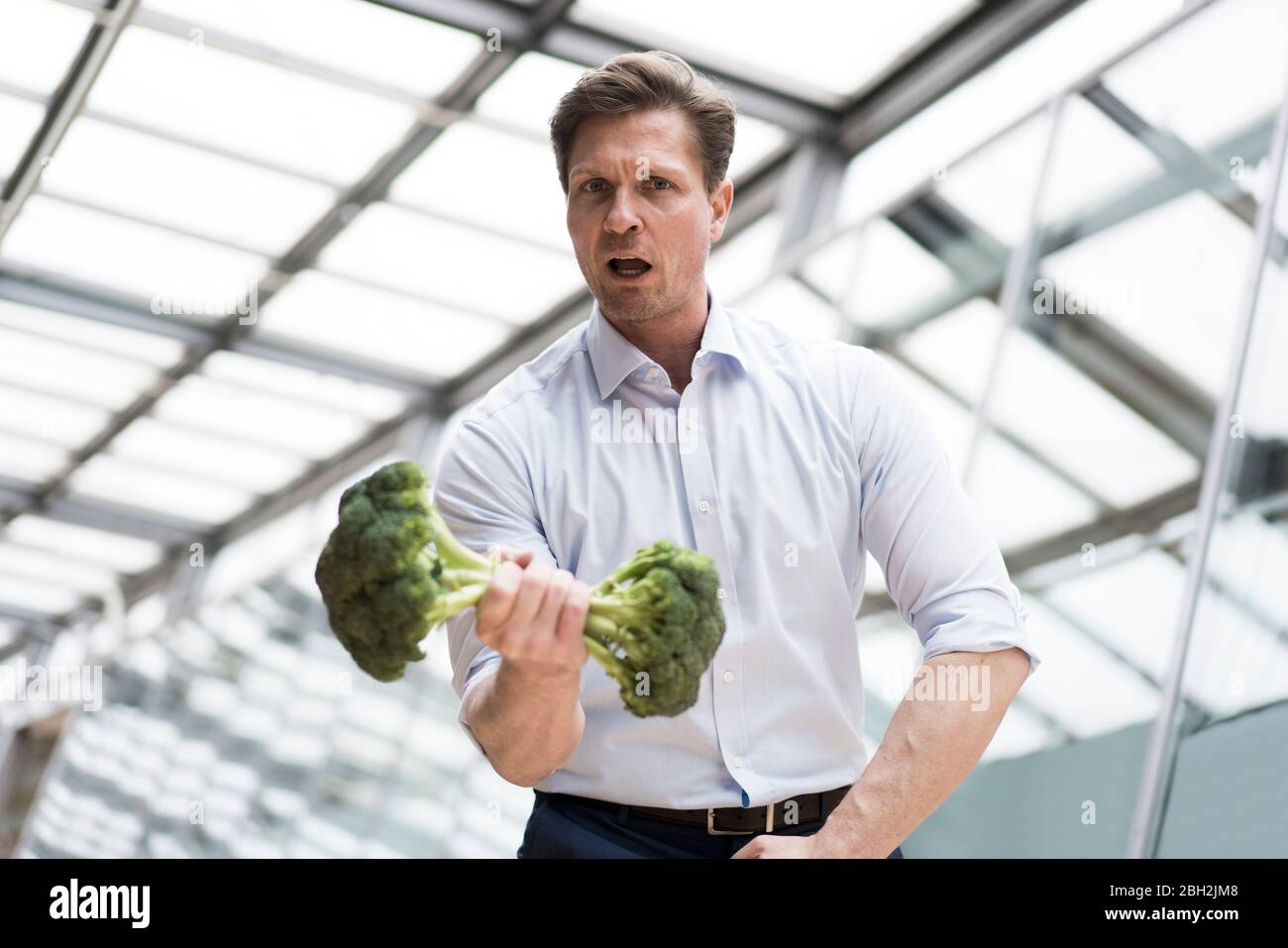 Uomo d'affari che fa l'addestramento del peso con broccoli Foto Stock