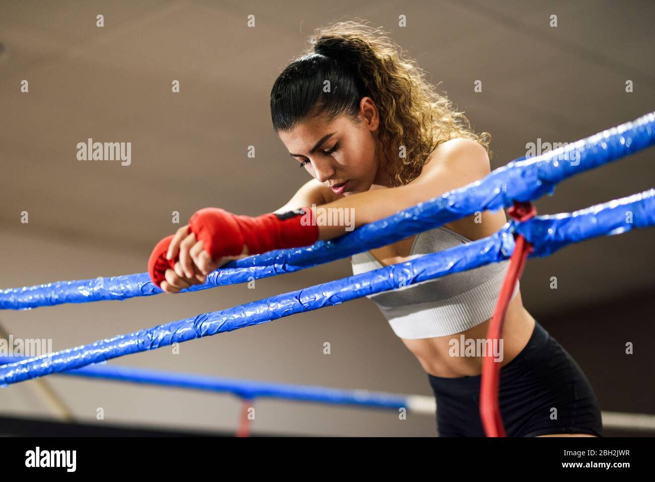 Pugile atletico femmina in pugilato anello poggiato su corda concentrandosi prima del combattimento Foto Stock