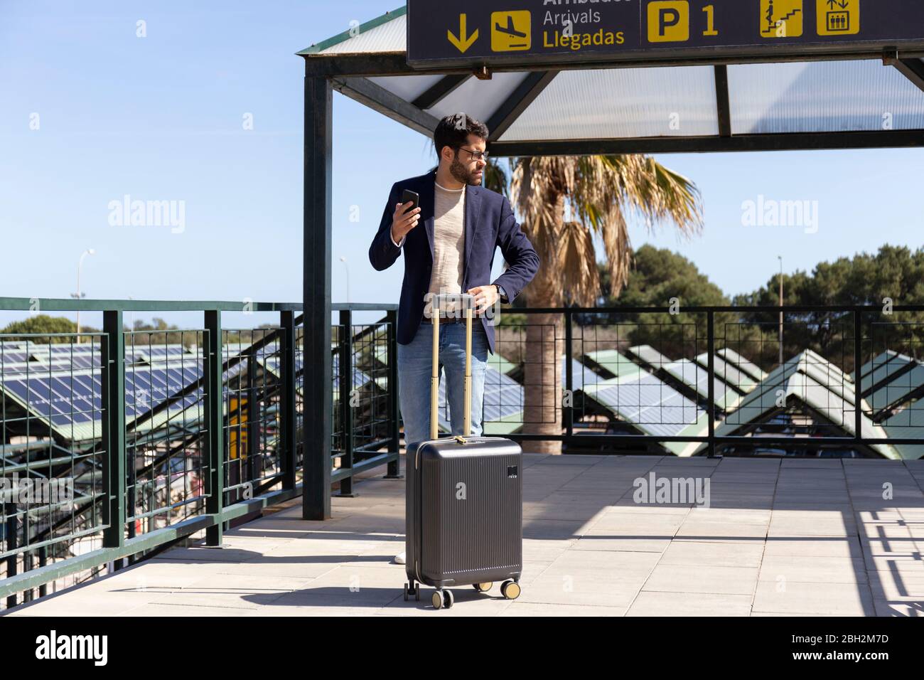 Uomo d'affari con smartphone e borsa trolley in piedi sulla terrazza sul tetto di un aeroporto Foto Stock