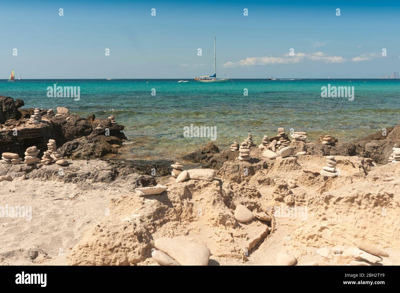 Vista panoramica sul mare con barche ormeggiate da una spiaggia con rocce sabbiose e pietre piramidali. Spiaggia di Formentera, Isole Baleari Spagna Foto Stock