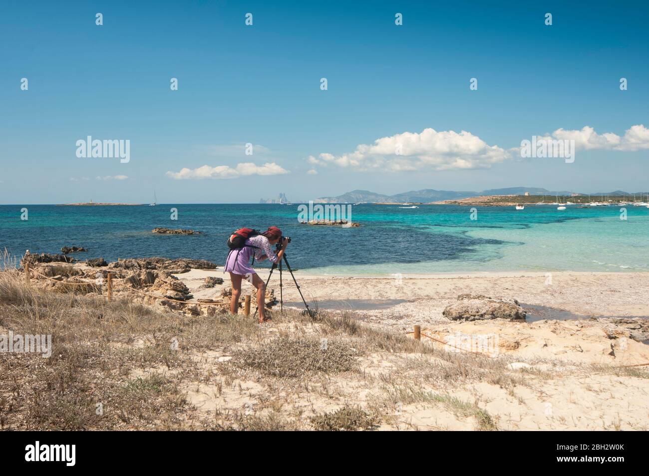 Una giovane donna irriconoscibile che scatta una foto con un cavalletto in una spiaggia di Formentera, Spagna Foto Stock