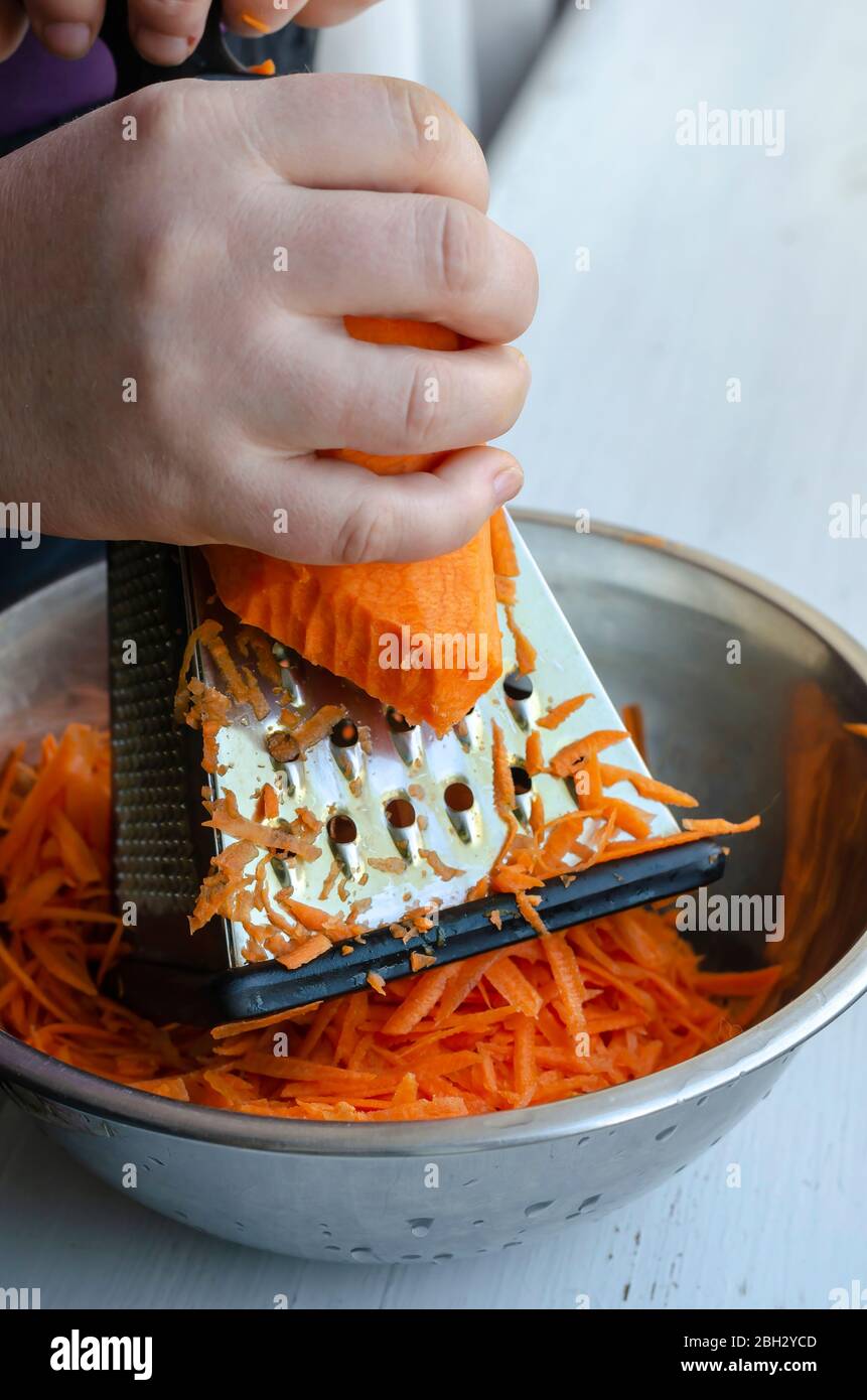 Donna macina le carote su un grattugia. Mano di una donna adulta trita una  verdura cruda