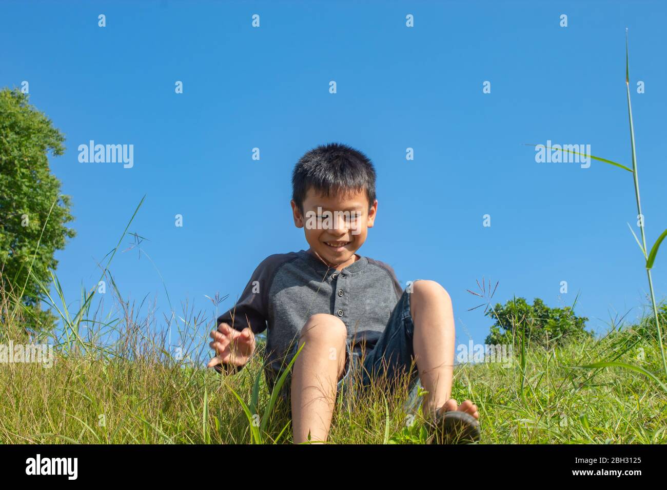Ragazzo asiatico sedersi sulla montagna erba collina Foto Stock