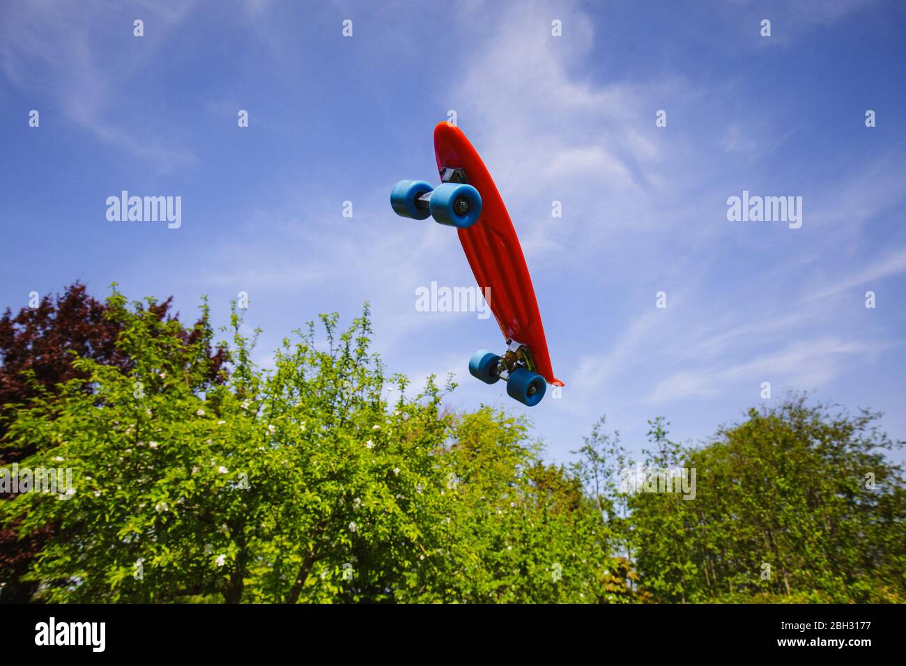 Uno skateboard rosso che si innalcia, gainst un cielo blu perfetto e alberi verdi Foto Stock