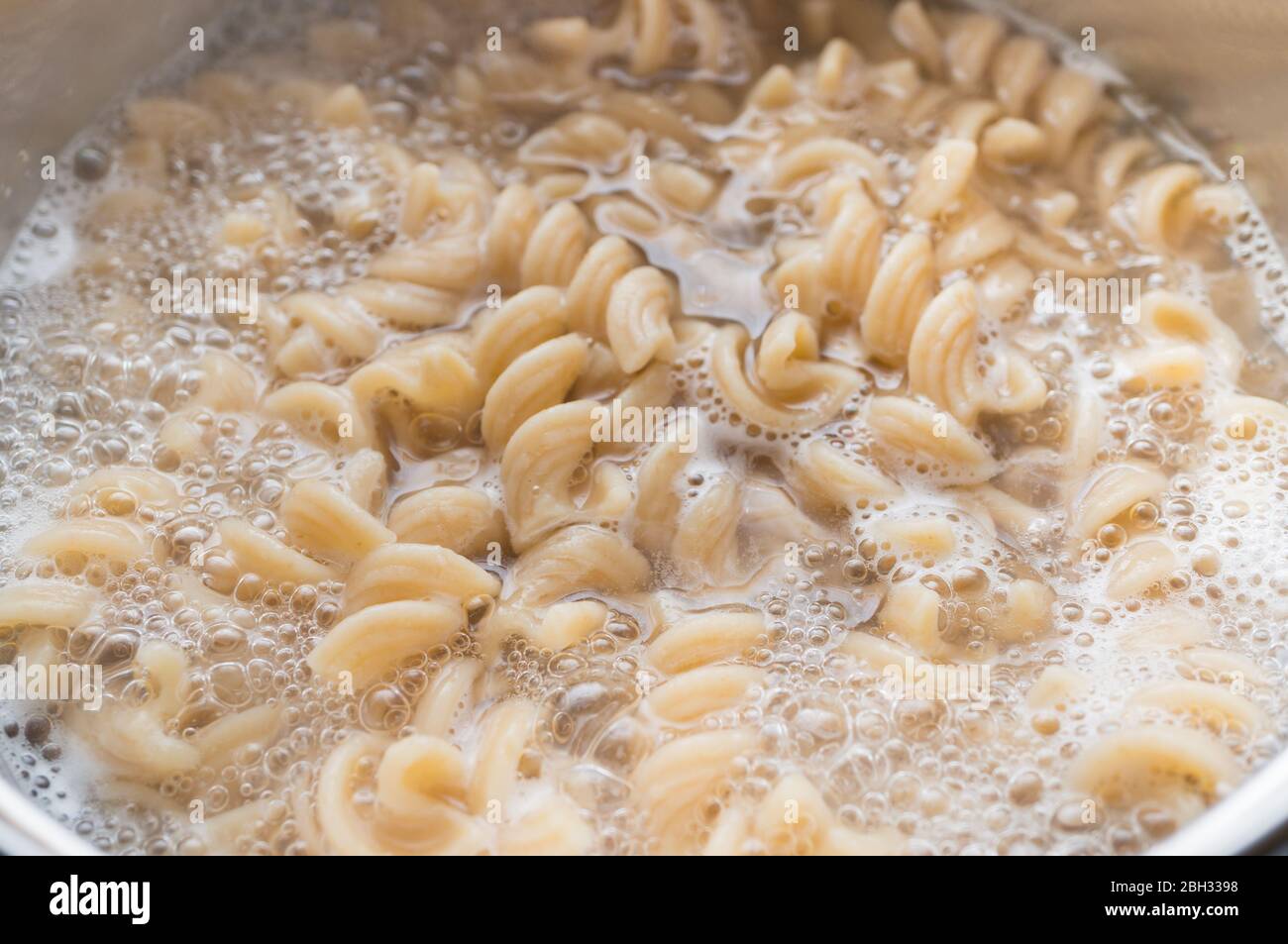 Pasta a grani interi in una padella con acqua bollente e un cucchiaio. Cucinare cibo sano Foto Stock