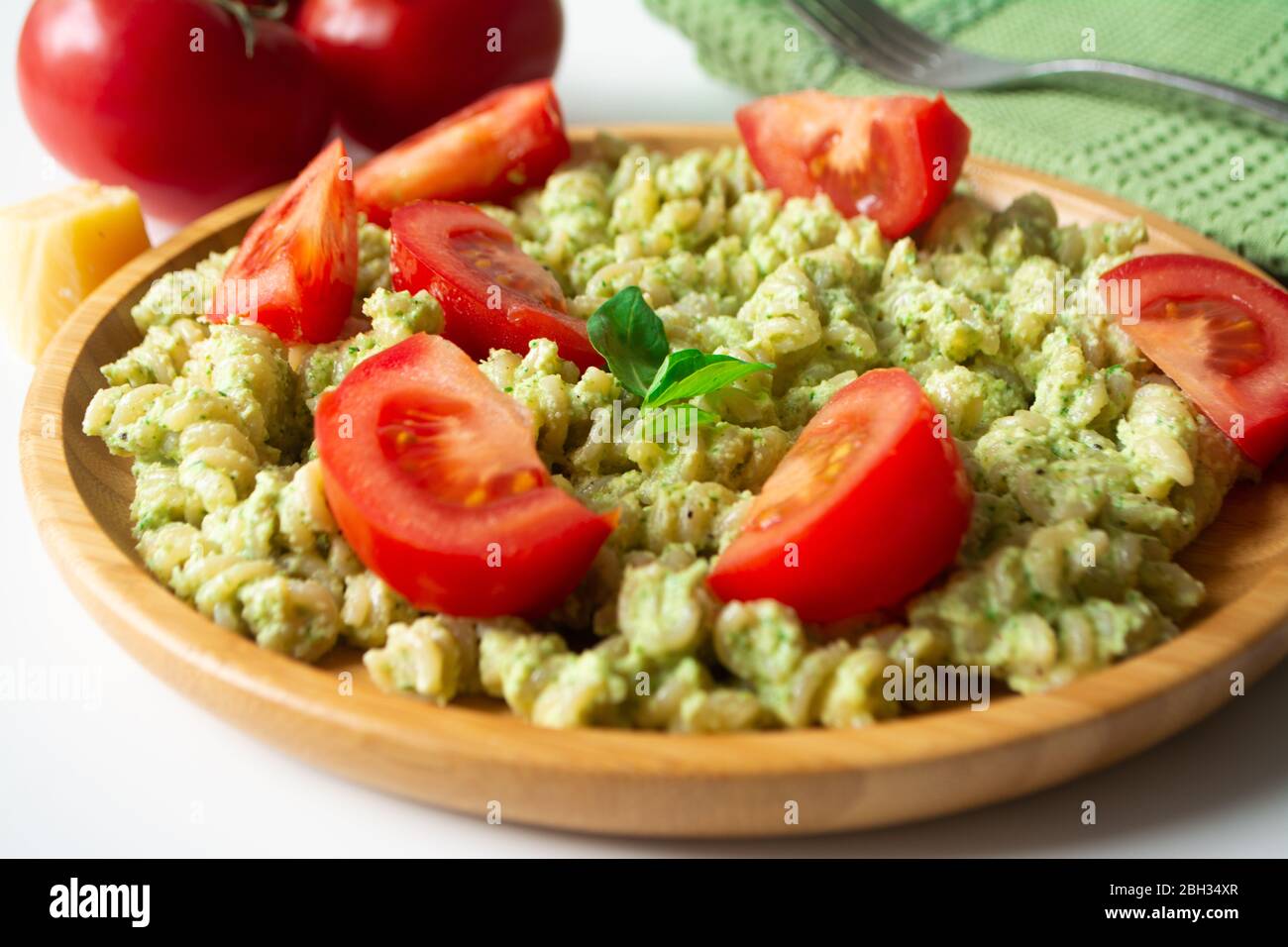 Pasta al basilico pesto fusilli con parmigiano e pomodori a fette in un piatto di legno e un tovagliolo verde con forchetta sullo sfondo Foto Stock
