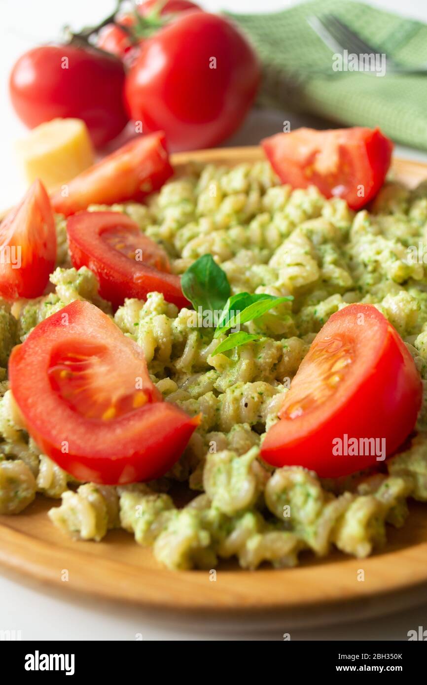 Pasta al basilico pesto fusilli con parmigiano e pomodori a fette in un piatto di legno e un tovagliolo verde con forchetta sullo sfondo Foto Stock