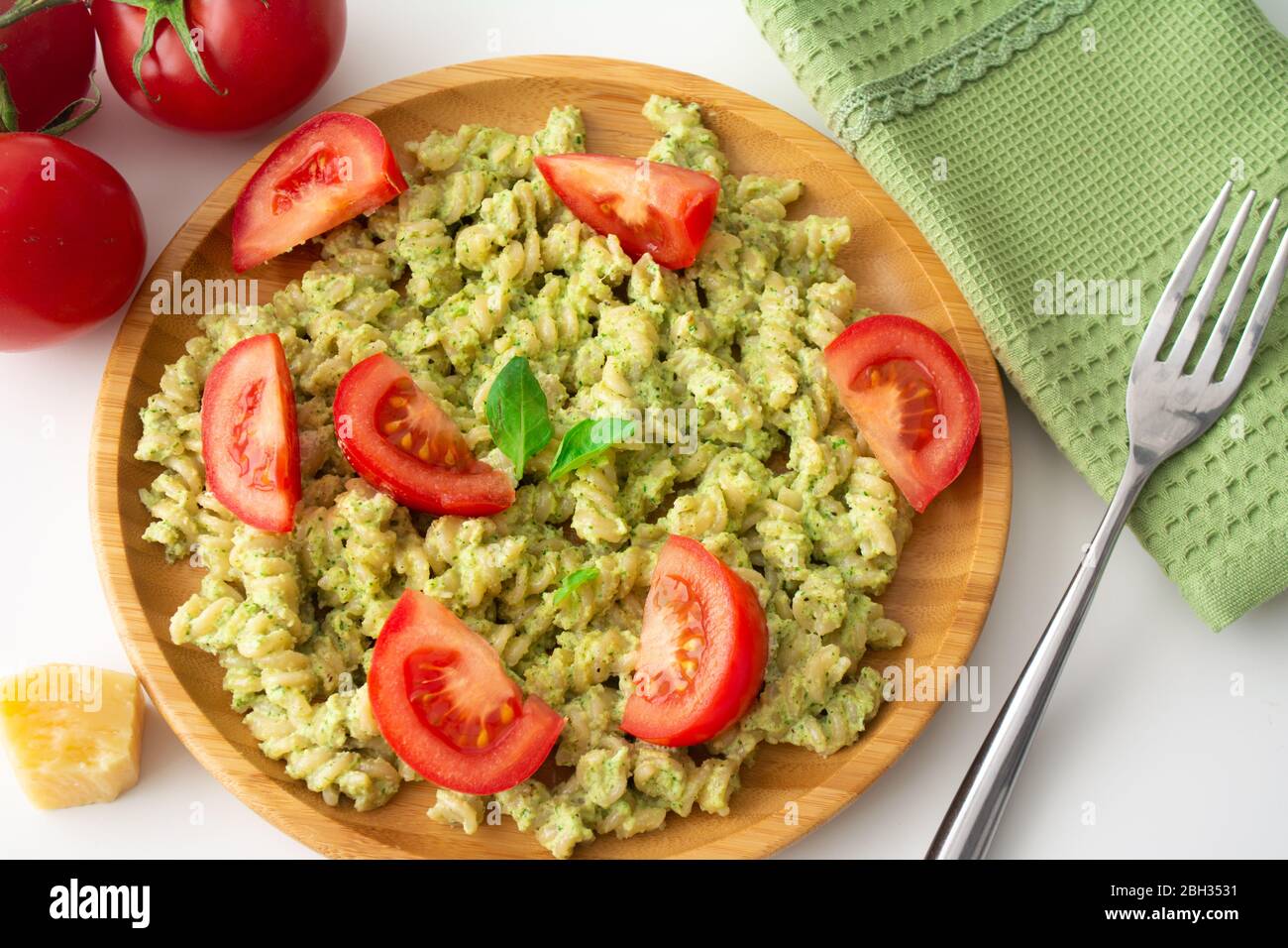Pasta al basilico pesto fusilli con parmigiano e pomodori a fette in un piatto di legno e un tovagliolo verde con forchetta sullo sfondo Foto Stock
