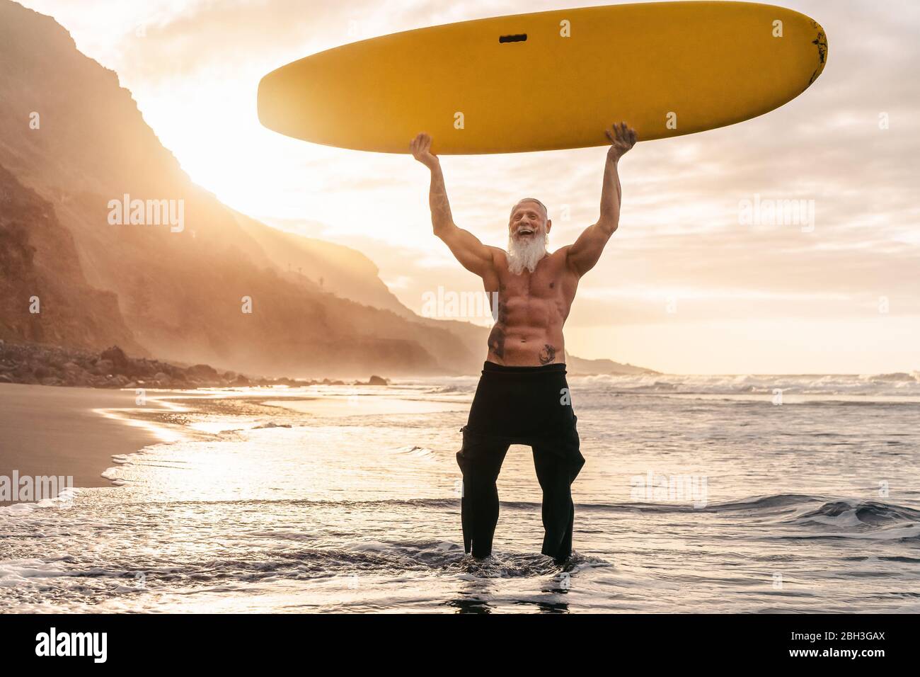 Happy FIT senior fun surfing al tramonto - allenamento sportivo da uomo con tavola da surf sulla spiaggia Foto Stock