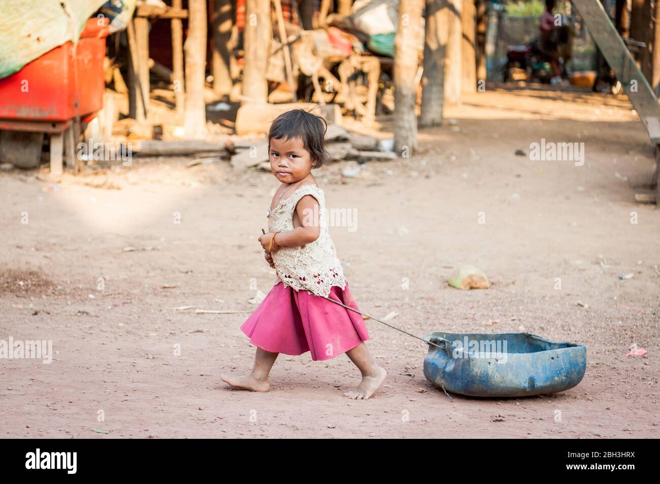 Una bambina cambogiana trascina il suo giocattolo lungo la strada principale al villaggio galleggiante di Kampong Phluk, vicino al lago Tonle SAP, Cambogia. Foto Stock