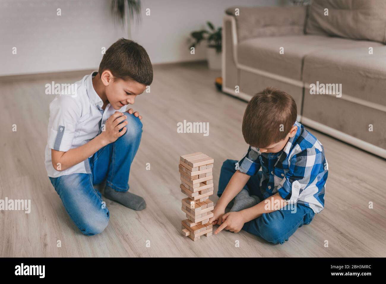 Due ragazzi fratelli costruiscono una torre di blocchi di legno della casa sul pavimento. Gioco da tavolo. Il concetto di quarantena familiare indipendente, infezione, coron Foto Stock