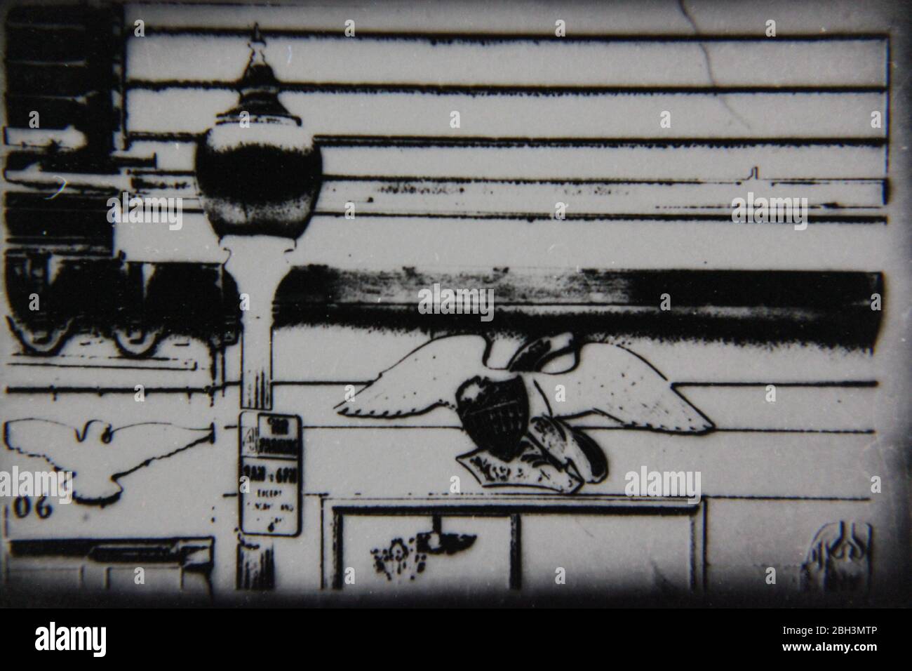 Fine anni '70 nero e bianco nero d'epoca fotografia estrema di una lampada da strada brillante e un'aquila scolpita appesa al muro Foto Stock
