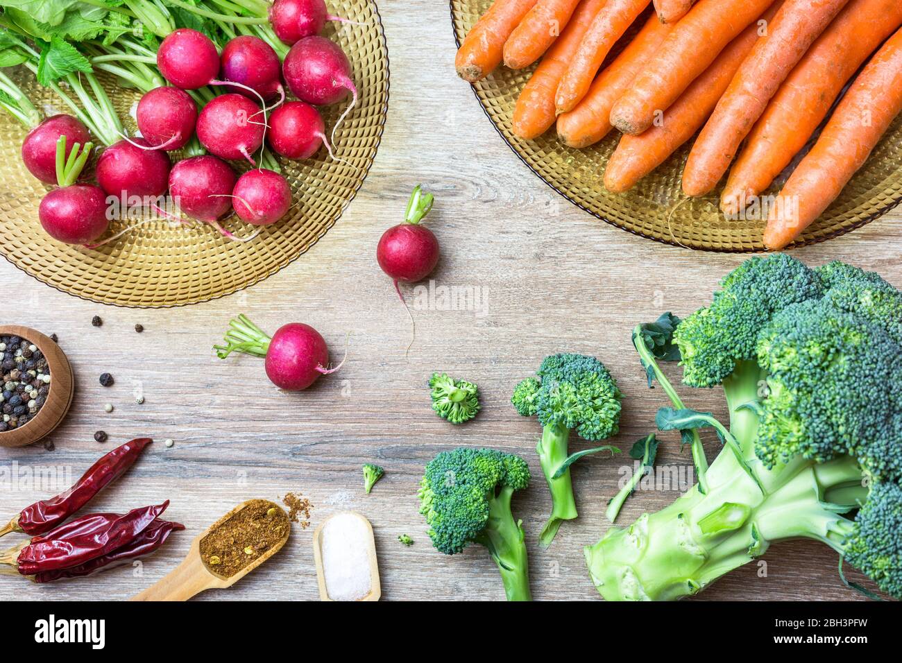 Freschi ravanelli rossi organici, carote, broccoli e spezie su sfondo legno. Vista dall'alto con spazio per le copie. Concetto di nutrizione sana. Foto Stock