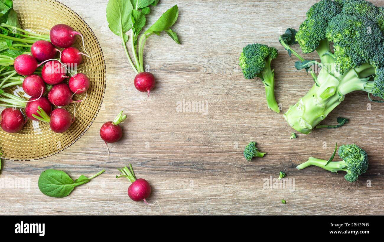 Ravanelli rossi e broccoli biologici freschi su sfondo legno. Vista dall'alto con spazio per le copie. Concetto di nutrizione sana. Foto Stock