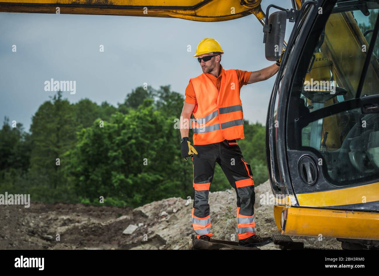 L'operatore dell'escavatore osserva il cantiere in piedi su attrezzature di movimento terra per impieghi gravosi. Foto Stock