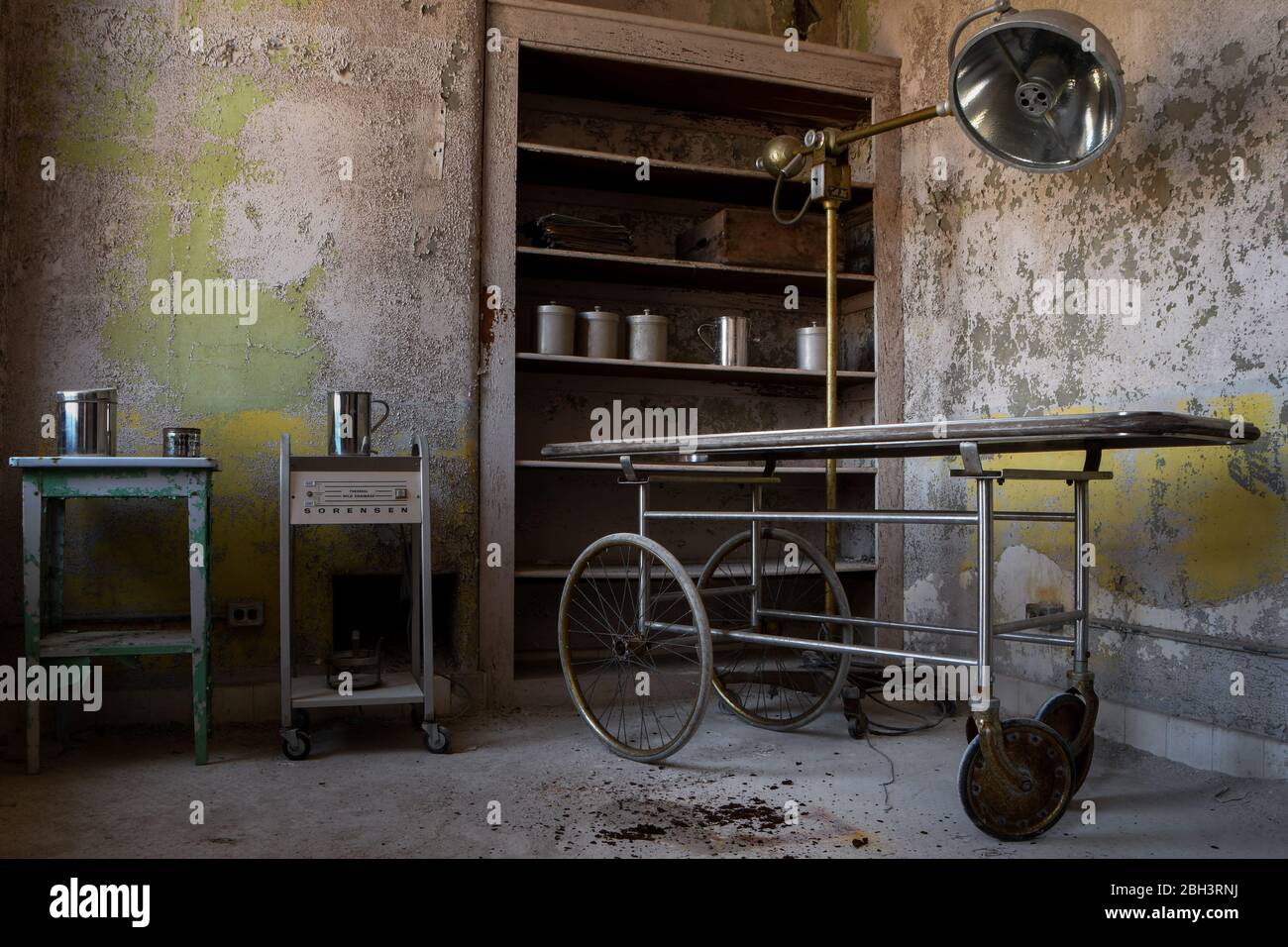 Apparecchiature mediche, tra cui un gurney, una lampada chirurgica e cartelle cliniche in un ospedale abbandonato Foto Stock