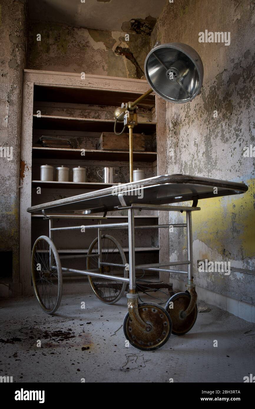 Apparecchiature mediche, tra cui un gurney, una lampada chirurgica e cartelle cliniche in un ospedale abbandonato Foto Stock