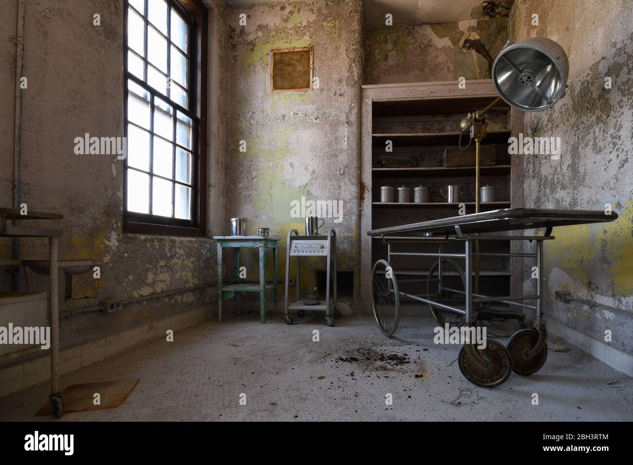 Apparecchiature mediche, tra cui un gurney, una lampada chirurgica e cartelle cliniche in un ospedale abbandonato Foto Stock