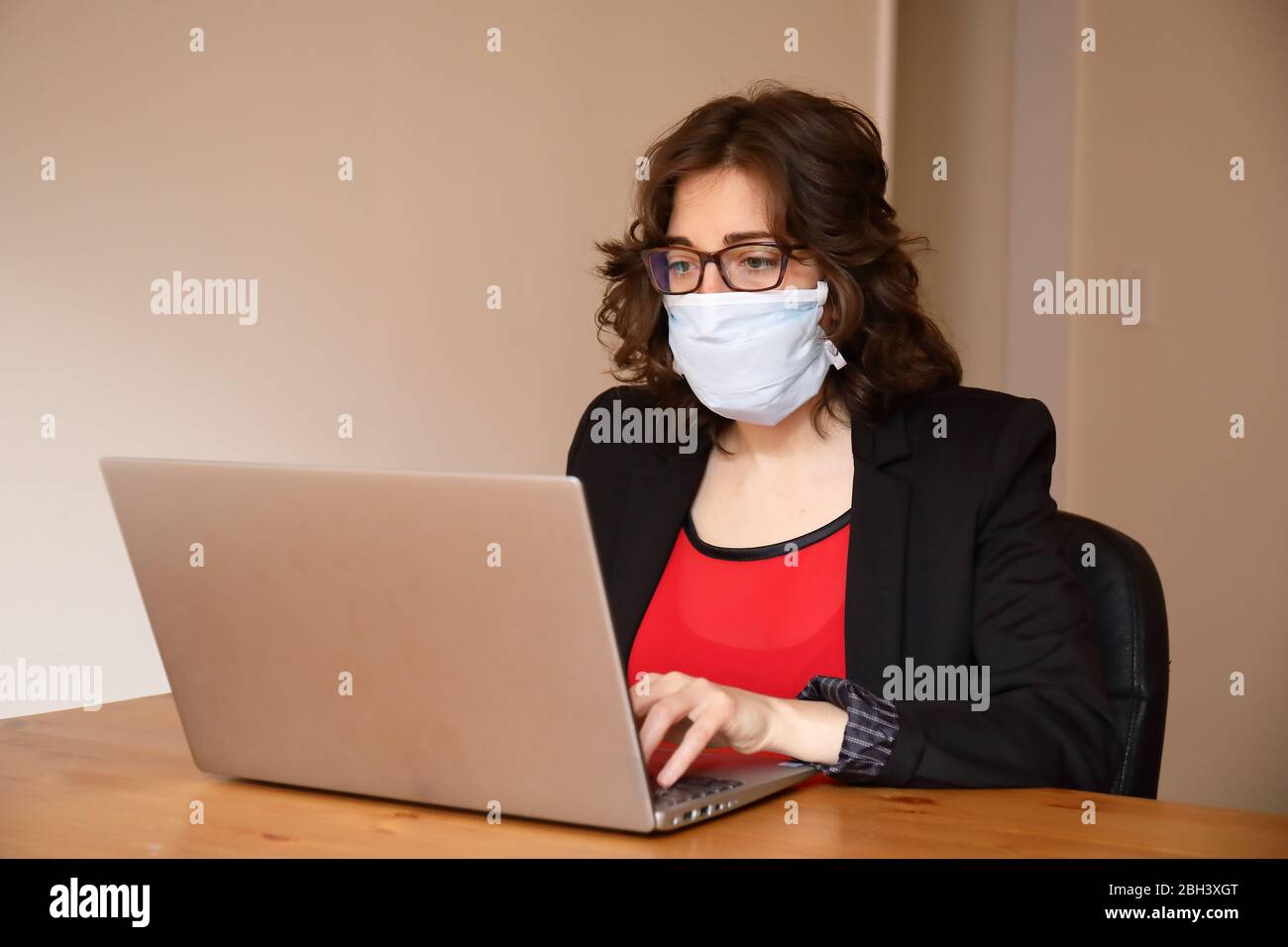 Una giovane e moderna donna d'affari sta lavorando nel laptop indossando giacca nera e t-shirt rossa con una maschera durante lo scoppio di Covid-19 Foto Stock