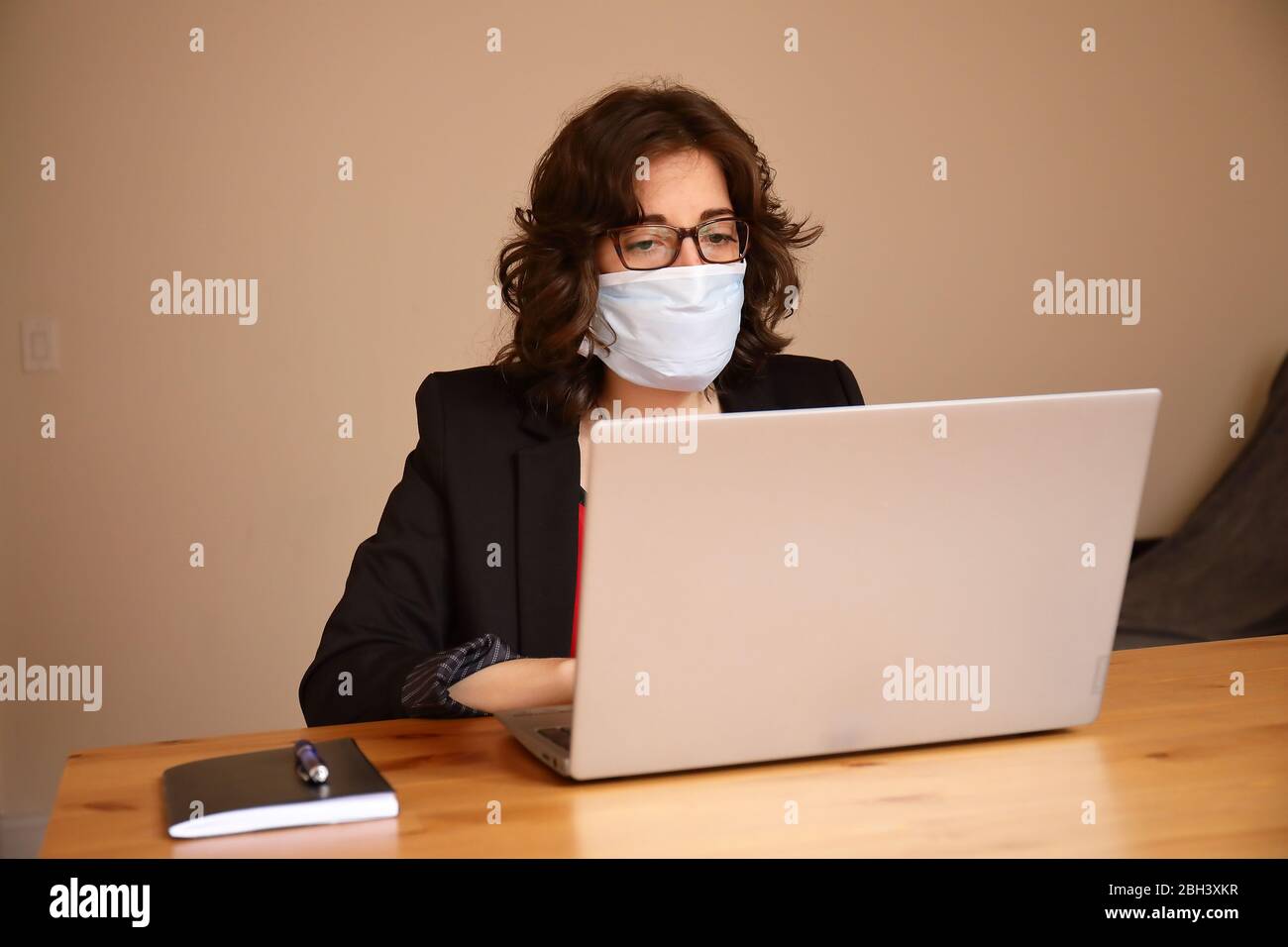 Una giovane e moderna donna d'affari sta lavorando nel laptop indossando giacca nera e t-shirt rossa con una maschera durante lo scoppio di Covid-19 Foto Stock