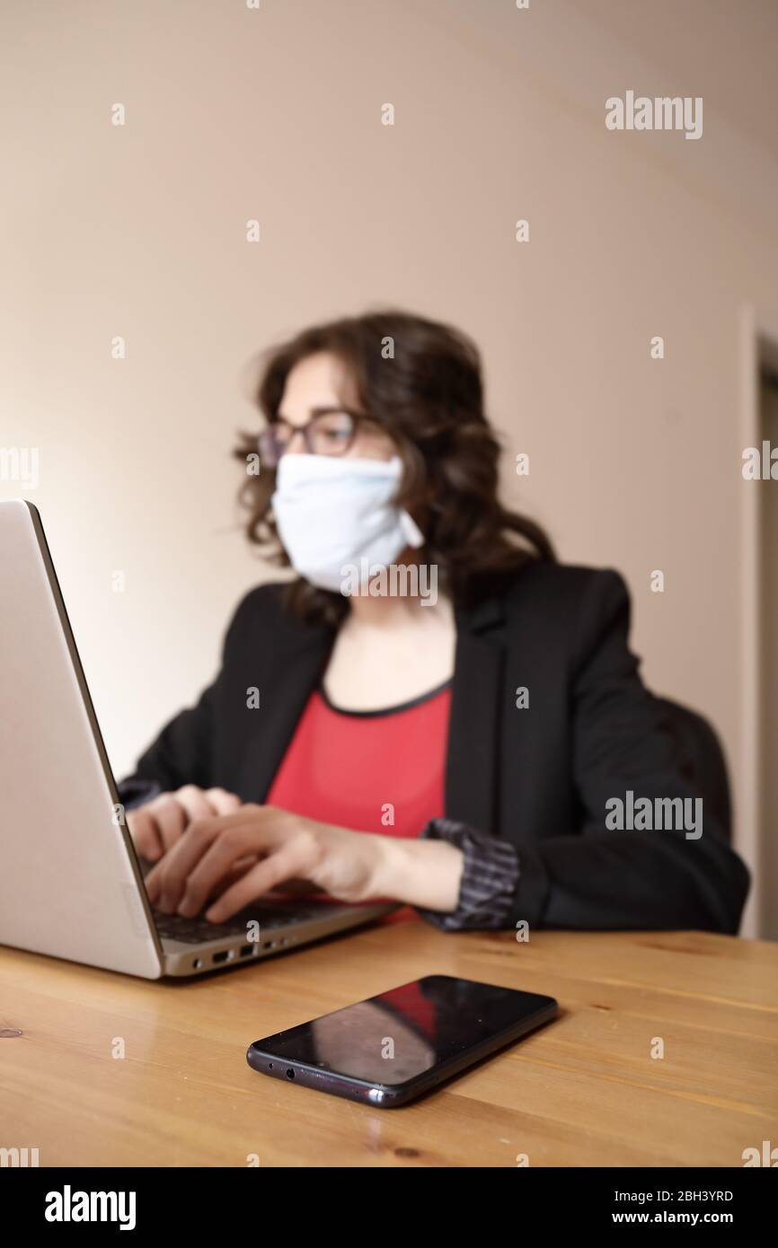 Una giovane e moderna donna d'affari sta lavorando nel laptop indossando giacca nera e t-shirt rossa con una maschera durante lo scoppio di Covid-19 Foto Stock