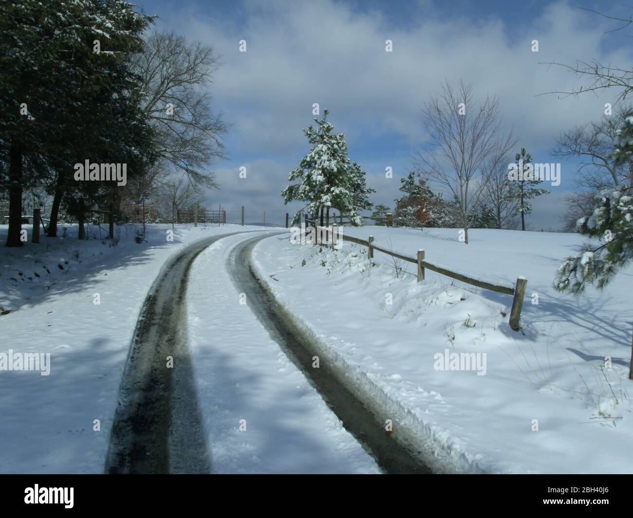 Le piste dei pneumatici scompaiono intorno a una curva e in un paesaggio invernale innevato su una strada di campagna Foto Stock