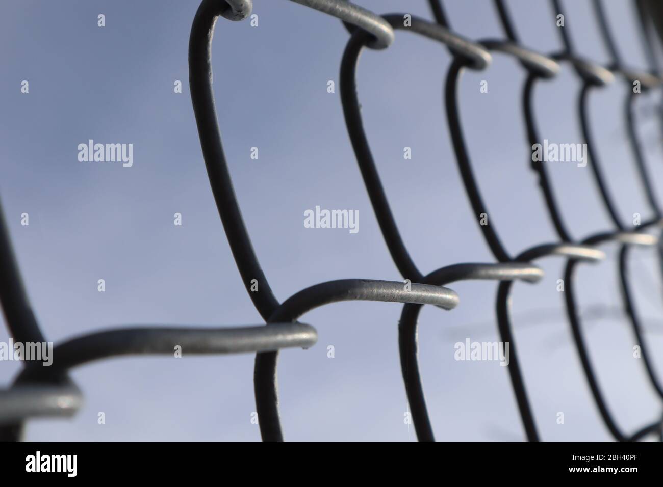 Vista prospettica in primo piano di una sezione di una fence di collegamento a catena contro un cielo blu, effetto bokeh Foto Stock