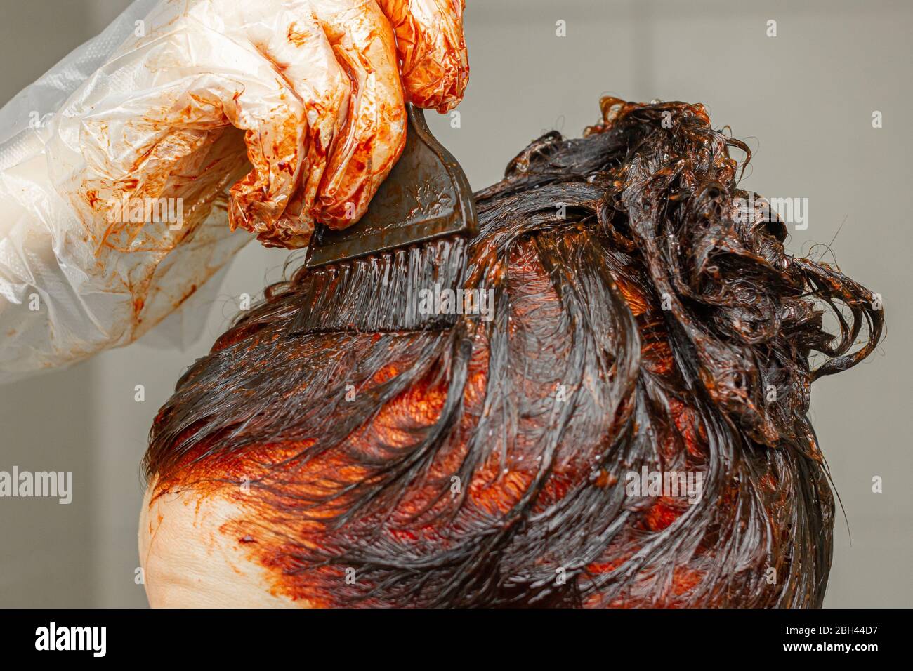 Processo di tintura dei capelli in rosso con un pennello. Giovane donna applicare un colore rosso ai capelli. Foto Stock