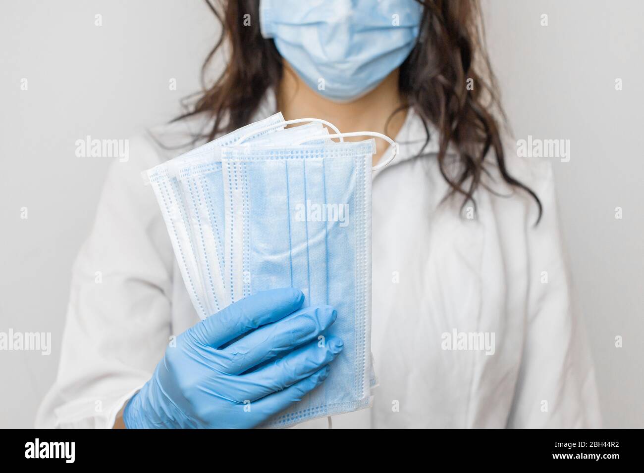 Arrestare SARSCoV, virus 2020, COVID-19. Le mani di Womans nei guanti medici blu che tengono una maschera protettiva. Medico che indossa la maschera facciale di protezione contro Foto Stock
