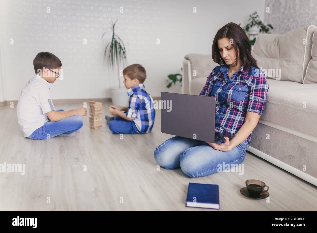 Rimani a casa, mamma che lavora in remoto su un notebook nel soggiorno mentre i bambini giocano. Compiti a casa. Concetto di distanza sociale. Quarantena. Chiudi, Foto Stock
