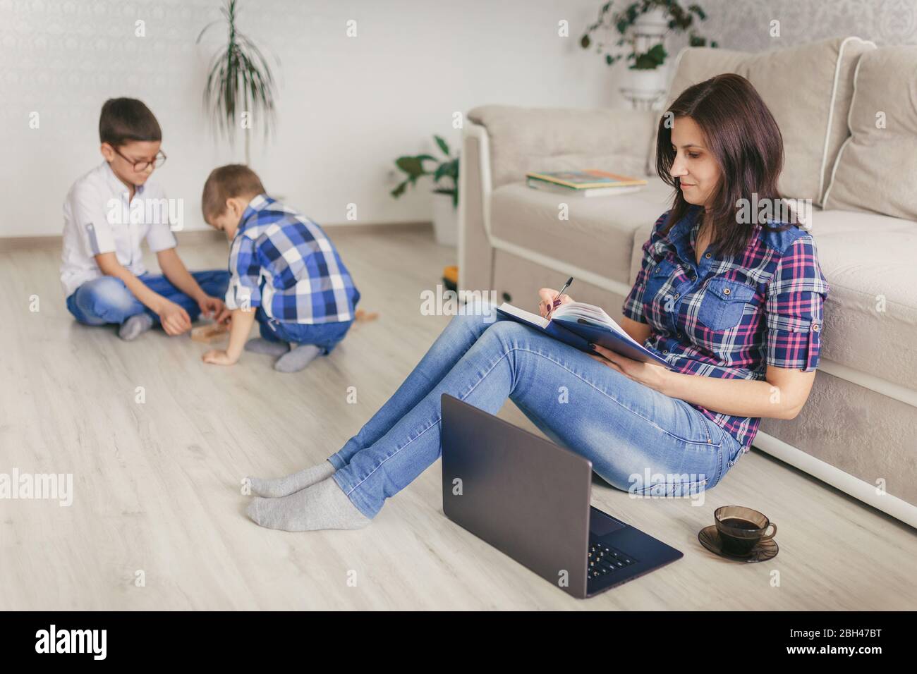 Rimani a casa, mamma che lavora in remoto su un notebook nel soggiorno mentre i bambini giocano. Compiti a casa. Concetto di distanza sociale. Quarantena. Chiudi, Foto Stock