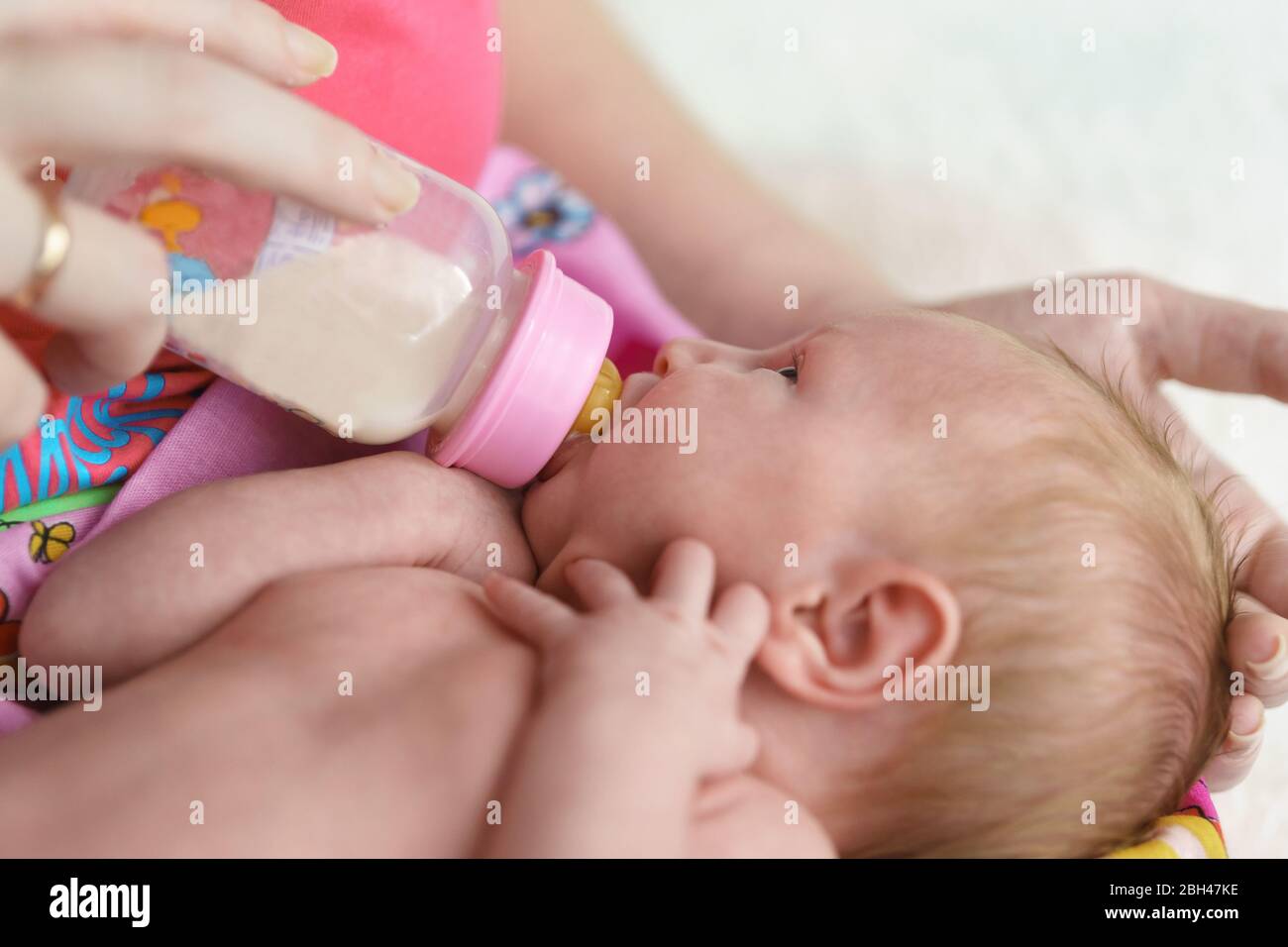 Una piccola ragazza neonato è nutrita formula da una bottiglia in braccia madri. Alimentazione artificiale Foto Stock