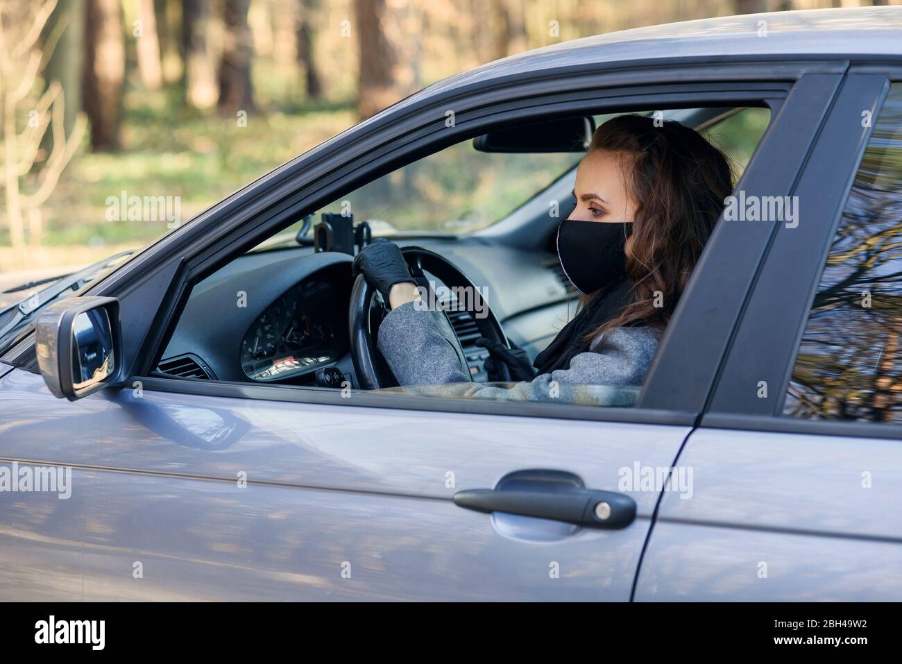 Donna d'affari in maschera facciale protettiva e guanti di gomma guidare un'auto. Protezione personale durante la quarantena. Mondo coronavirus pandemico, PR personale Foto Stock