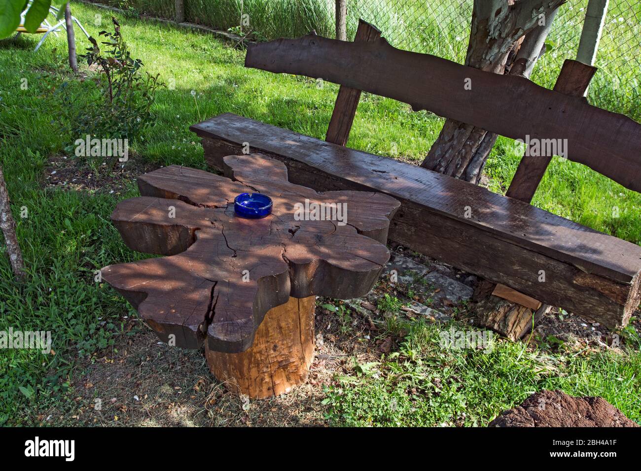 Posto tranquillo e tranquillo in un piccolo parco con panca e tavolo in legno. La panchina e il tavolo all'ombra sono in attesa di visitatori. Foto Stock
