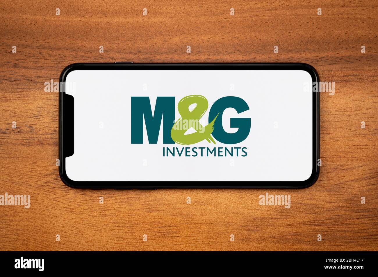 Uno smartphone con il logo M&G Investments si appoggia su un tavolo di legno semplice (solo per uso editoriale). Foto Stock