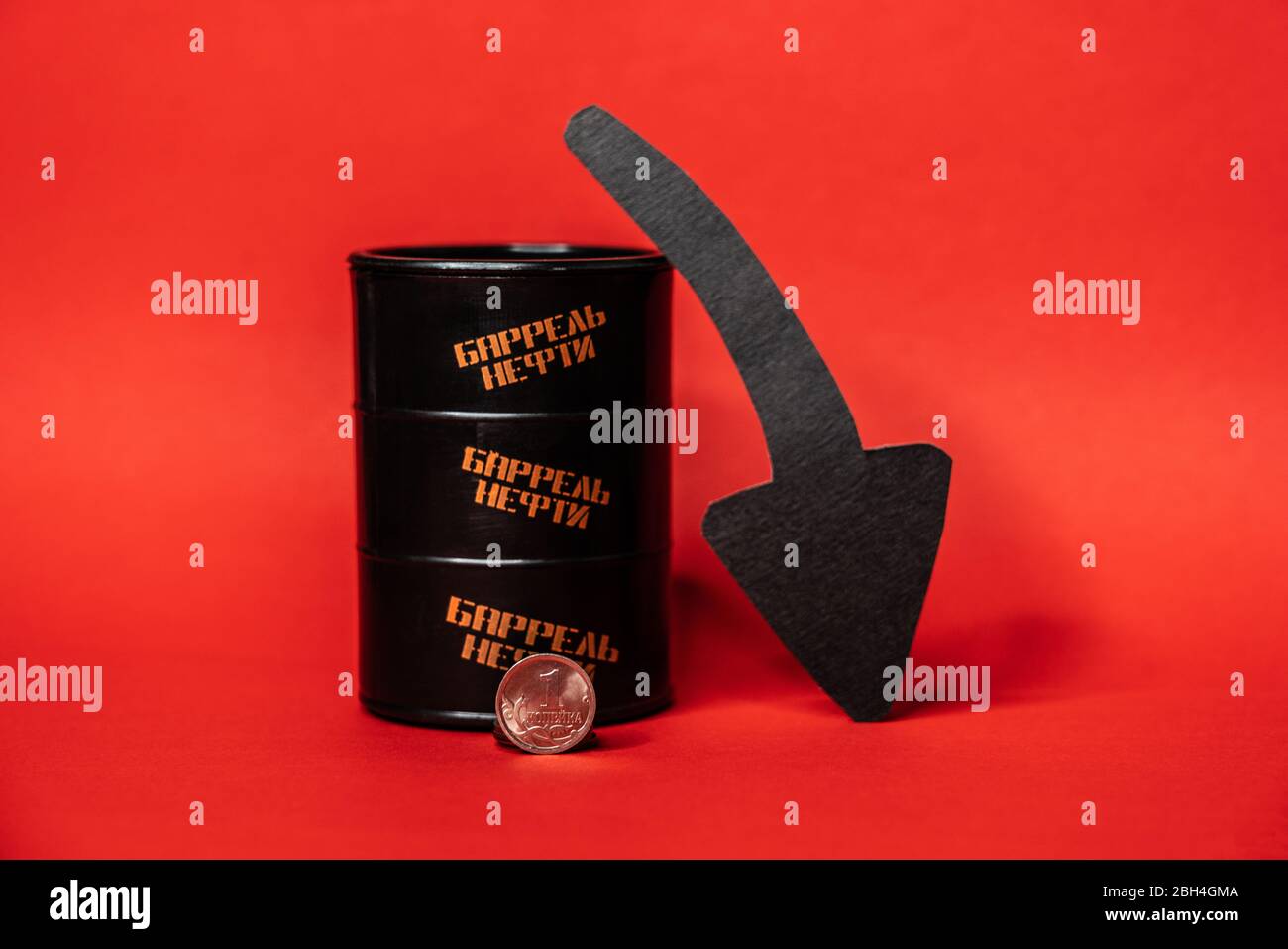 Barile nero con una moneta da un solo centesimo e freccia giù su sfondo rosso. Il prezzo al barile del petrolio scende sotto grafico. Andamento del mercato petrolifero. Infogra di petrolio Foto Stock