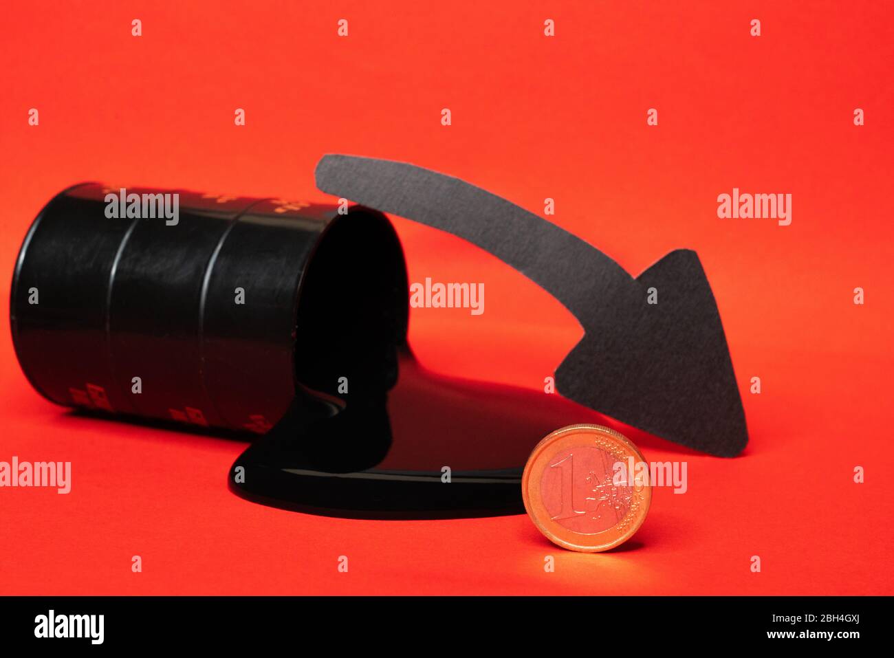 olio che fuoriesce dal barile con una moneta da un euro e una freccia giù su sfondo rosso. Il prezzo al barile del petrolio scende sotto grafico. Andamento del mercato petrolifero. Petrolio Foto Stock