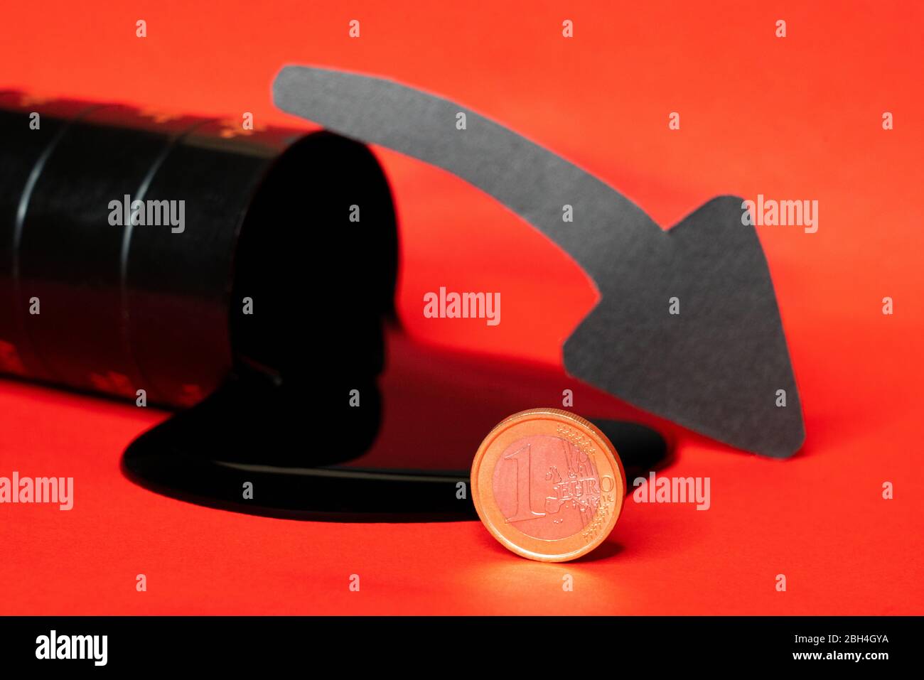 olio che fuoriesce dal barile con una moneta da un euro e una freccia giù su sfondo rosso. Il prezzo al barile del petrolio scende sotto grafico. Andamento del mercato petrolifero. Petrolio Foto Stock