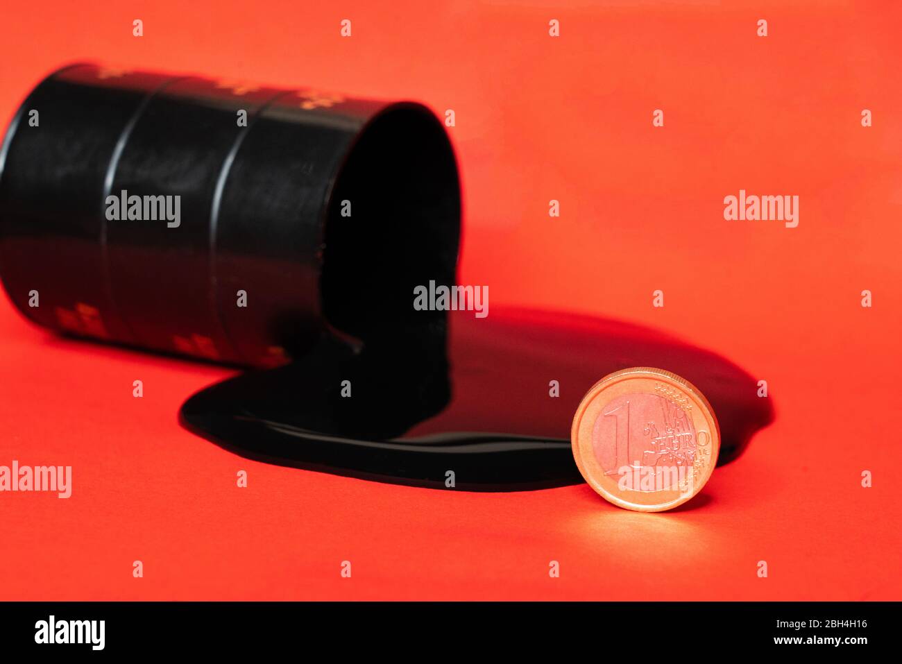il petrolio che fuoriesce dal barile con una moneta da un euro su sfondo rosso. Il prezzo al barile del petrolio scende sotto grafico. Andamento del mercato petrolifero. Infografica sul petrolio. Foto Stock