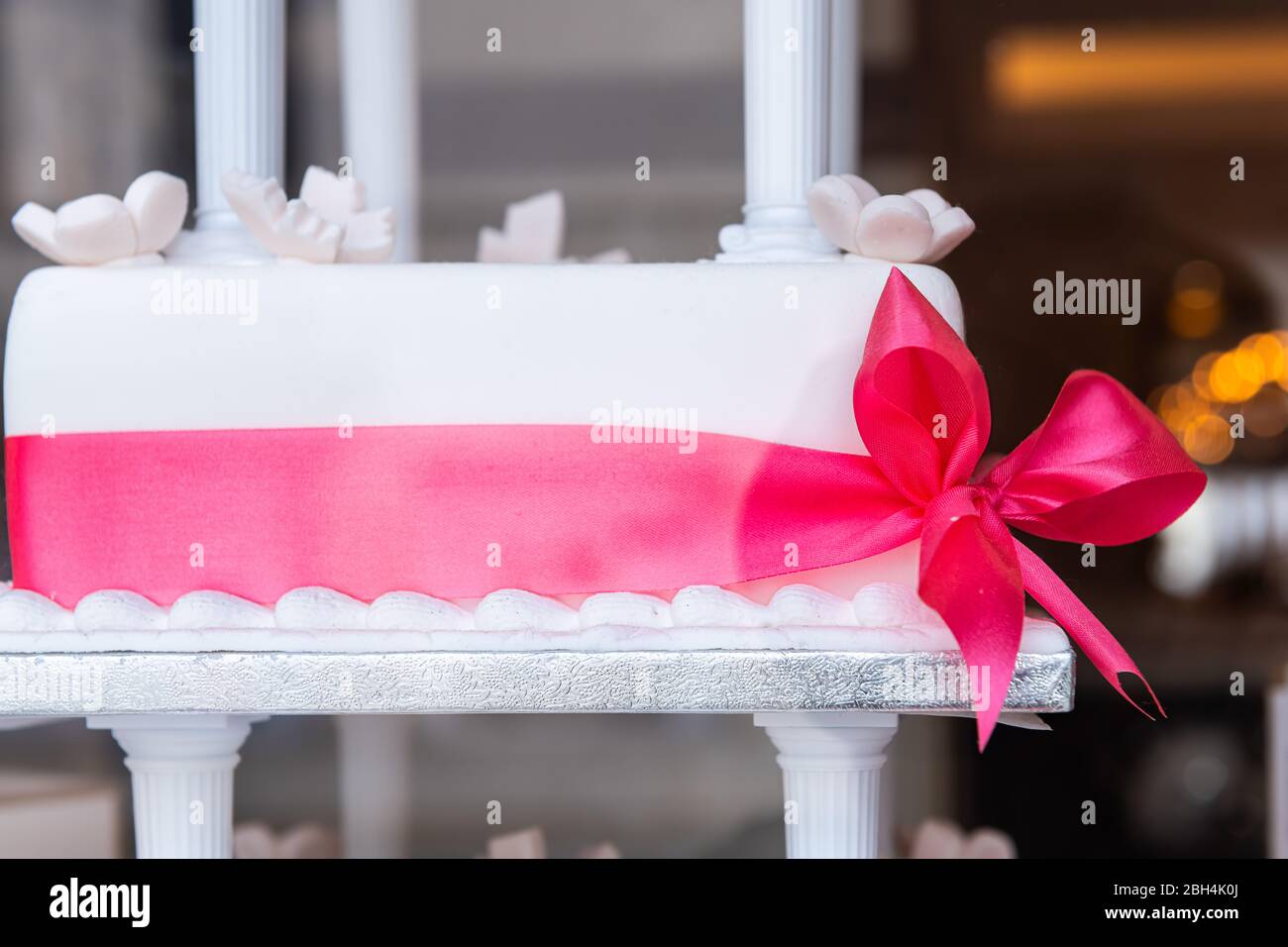 Primo piano di torta nuziale bianca a graticcio con decorazione a nastro rosa sullo stand vista attraverso la finestra del forno Foto Stock