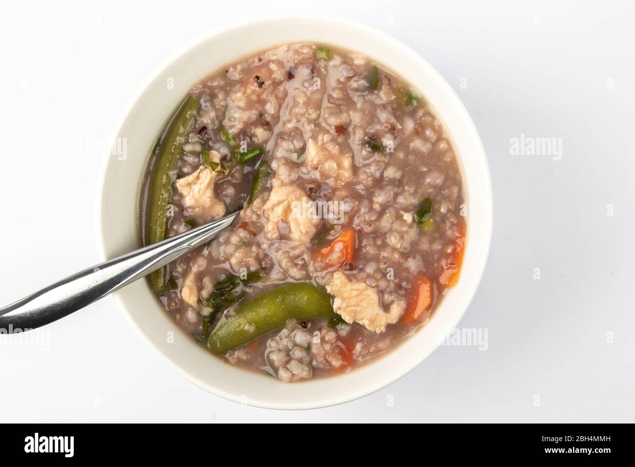 Delizioso porridge di riso marrone fatto in casa con poche fette di pollo, carota e verdure isolate su sfondo bianco. Foto Stock
