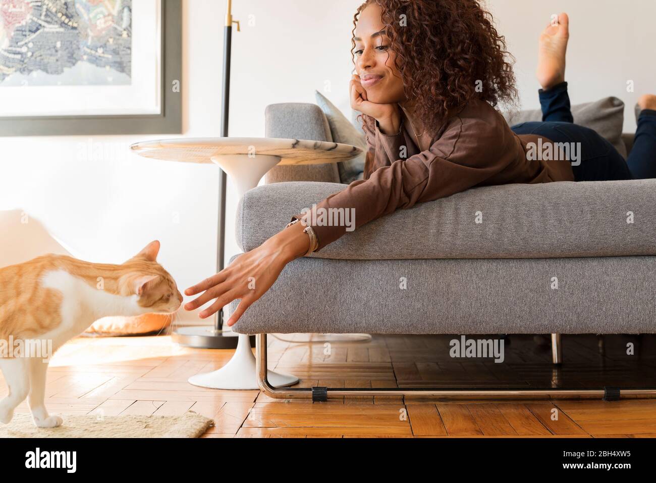 Donna sorridente sul divano che raggiunge il gatto Foto Stock